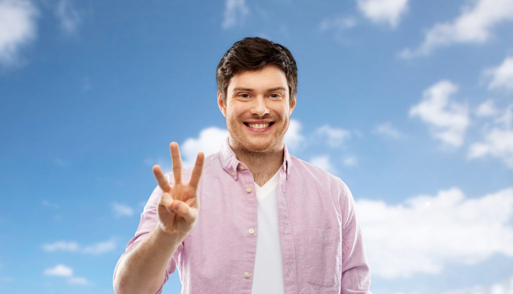 count and people concept - smiling young man showing three fingers over blue sky and clouds background