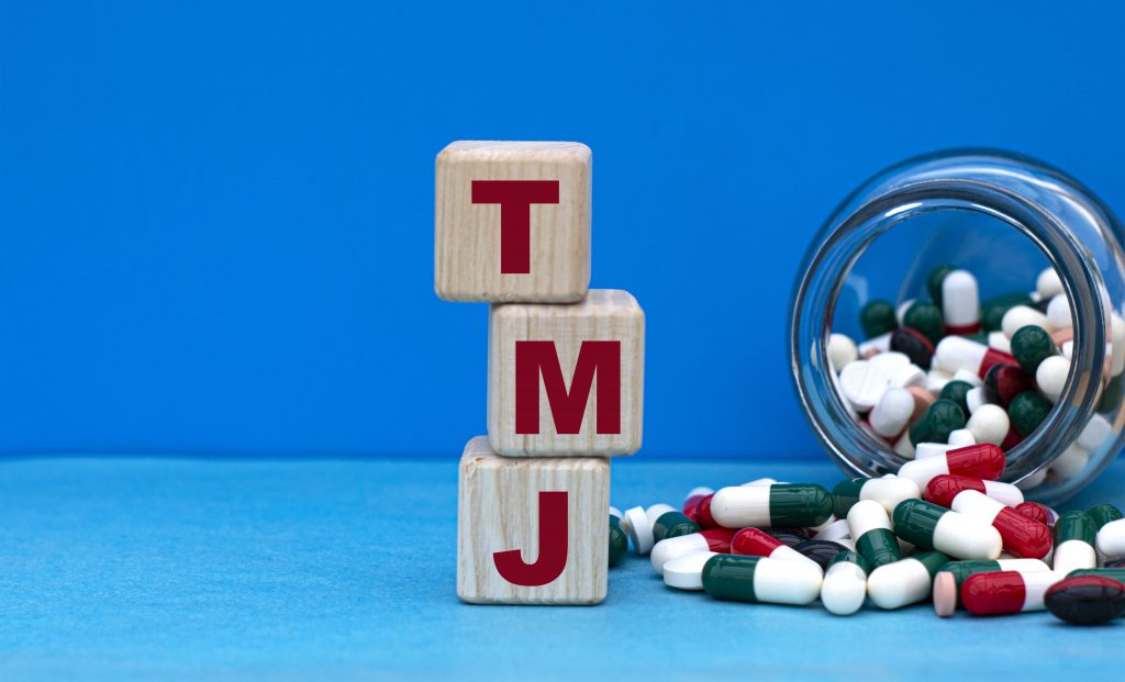 TMJ word on cubes on a blue background with a jar of tablets. Medical concept.