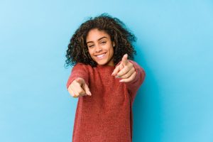 Young african american curly hair woman cheerful smiles pointing to front.