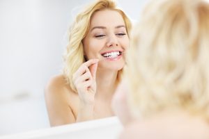 A picture of a young happy woman using dental floss in the bathroom