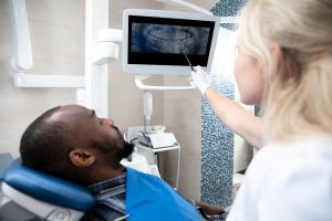 Young african-american man visiting dentist's office for prevention and treatment of the oral cavity. Man and woman doctor while checkup teeth. Healthy lifestyle, healthcare and medicine concept.