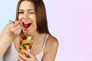 Young woman eating fruits from glass on