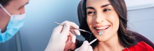 Wonderful treatment. Dentist in ear loop face mask and gloves is holding dental instruments and checking the result of his professional work in the dental center.