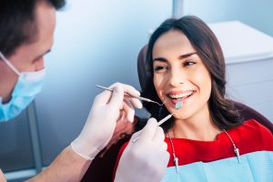 Wonderful treatment. Dentist in ear loop face mask and gloves is holding dental instruments and checking the result of his professional work in the dental center.