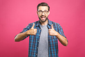 Portrait of young man in glasses showing thumbs up isolated over pink background
